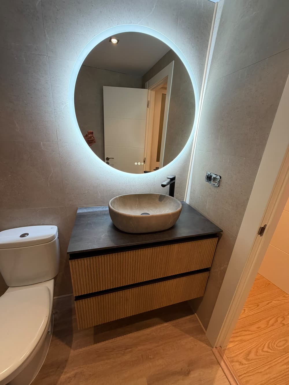 Baño reformado con espejo redondo con luz, mueble de lavabo suspendido e inodoro